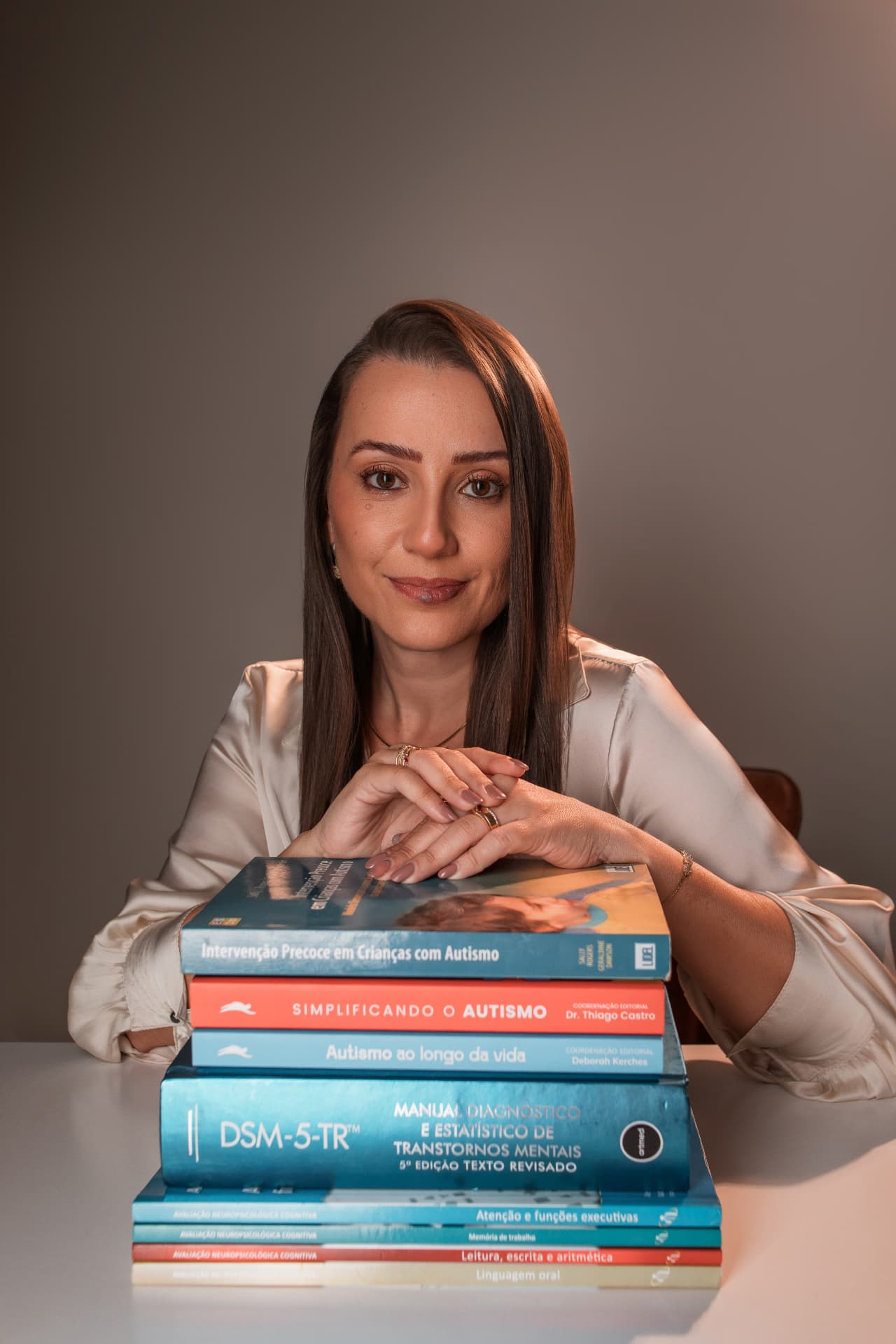 Naiara, educadora e especialista em ABA, com mãos entrelaçadas sobre uma pilha de livros